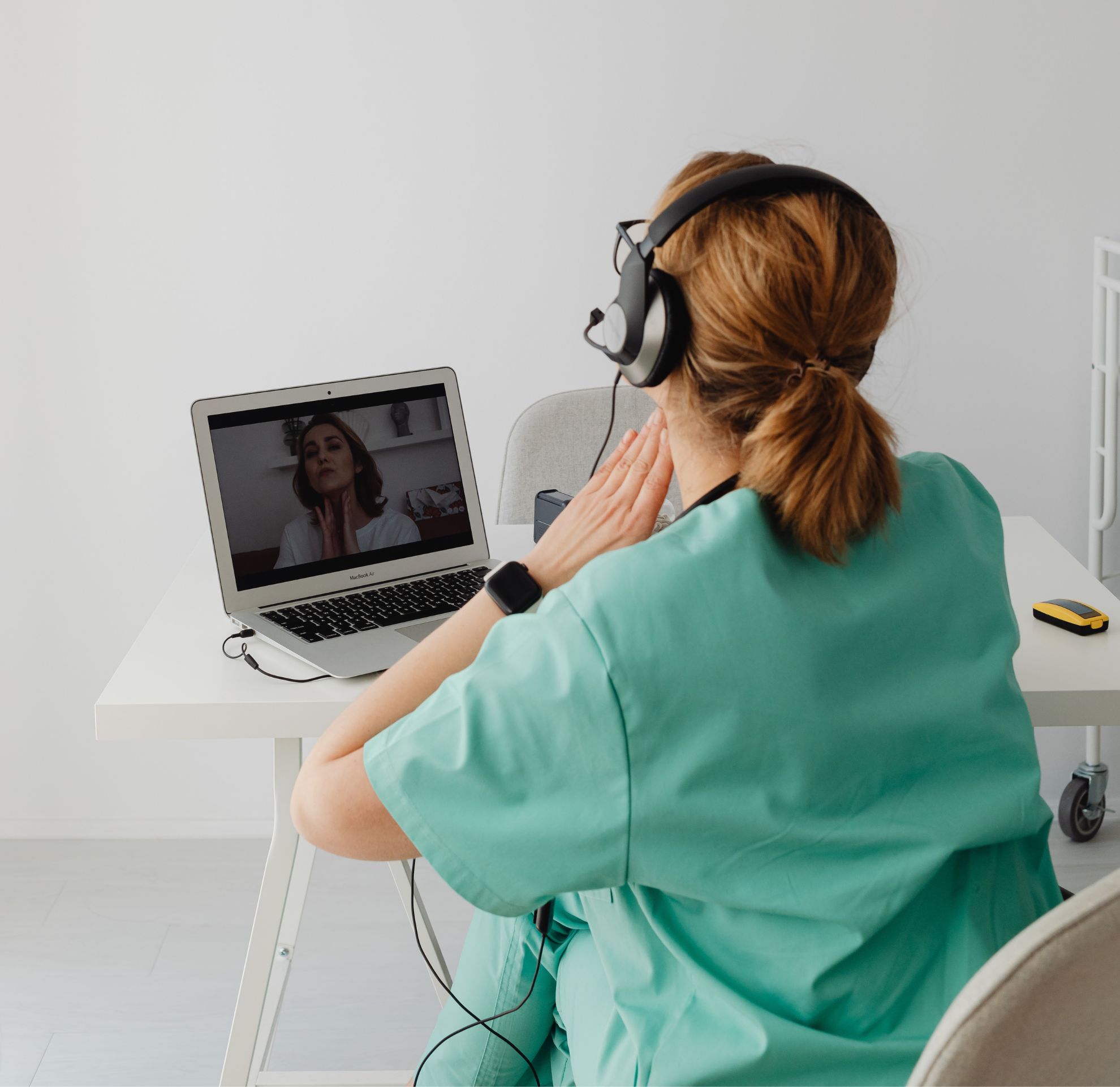 Profissional de saúde em consulta por vídeo no notebook, usando fones de ouvido, em ambiente claro.